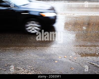 Nasse Stadtstraße nach dem Schmelzen des ersten Schnees und schwarz Auto verschwommen in Bewegung am Herbsttag Stockfoto