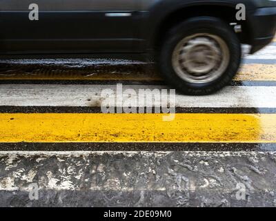 Nass nach dem Schmelzen der erste Schnee gelb und weiß gestreift Fußgängerüberweg und verschwommen in Bewegung Auto in der Stadt auf Herbsttag Stockfoto