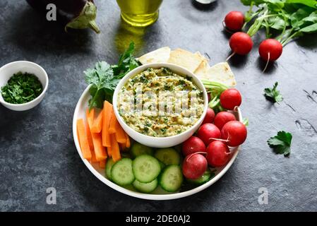 Baba ganoush (geröstete Auberginen-Dip) in Schüssel und frisches Bio-Gemüse auf blauem Stein Hintergrund. Gesunde Ernährung. Vegetarisches veganes Lebensmittelkonzept. Stockfoto