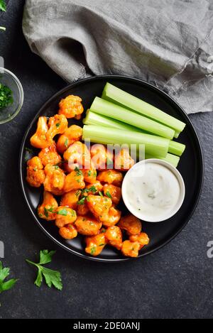 Büffelflügel aus Blumenkohl mit Sellerie und Sauce auf Platte über schwarzem Steingrund. Gesundes Essen, pflanzliches Lebensmittelkonzept. Draufsicht, flacher Lay Stockfoto