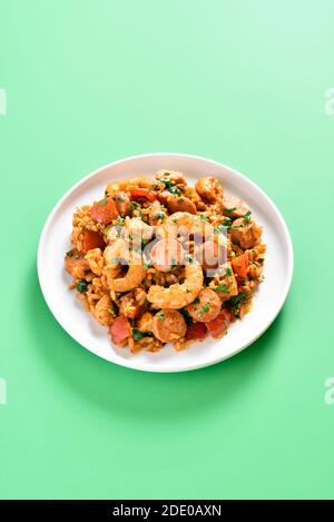 Kreolische Jambalaya mit Huhn, geräucherten Würstchen, Reis und Gemüse auf Teller auf grünem Hintergrund mit Kopierplatz. Stockfoto