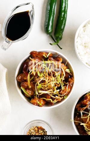 Würziges, im Knoblauch gebratenes Huhn (Kkanpunggi). Asiatisches Huhn in süß-saurer Sauce in Schüssel auf weißem Hintergrund. Draufsicht, flaches Lay Stockfoto