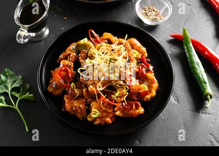 Würziger Knoblauch gebratenes Huhn (Kkanpunggi). Asiatisches Huhn in süßer und saurer Sauce auf Teller über schwarzem Stein Hintergrund. Stockfoto