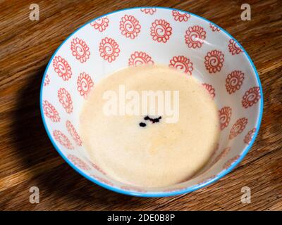 Kochen süßen Biskuitkuchen zu Hause - Draufsicht auf Flüssiger Teig mit Tropfen lila Lebensmittelfarbe in Schüssel Auf altem Holztisch in der heimischen Küche Stockfoto