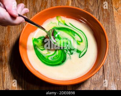 Kochen süßen Biskuitkuchen zu Hause - Draufsicht auf Rühren der grünen Lebensmittelfarbe in der Schüssel des flüssigen Teiges auf Alte Holztisch in der heimischen Küche Stockfoto