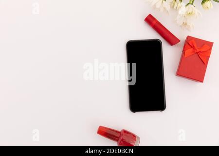 Smartphone, roter Lippenstift, Nagellack, Geschenk und Blumen auf weißem Hintergrund Stockfoto