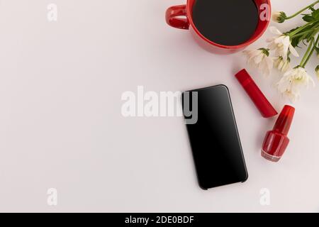 Smartphone, roter Lippenstift, Nagellack, Kaffee und Blumen auf weißem Hintergrund Stockfoto