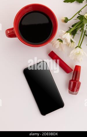 Smartphone, roter Lippenstift, Nagellack, Kaffee und Blumen auf weißem Hintergrund Stockfoto