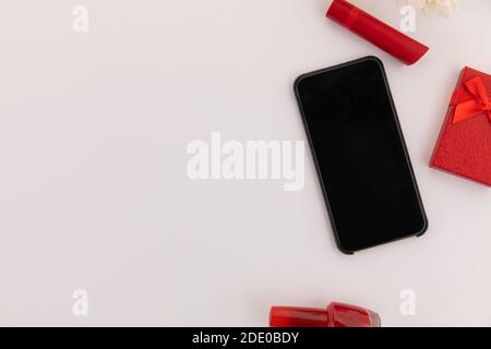 Smartphone, roter Lippenstift, Nagellack, Geschenk und Blumen auf weißem Hintergrund Stockfoto