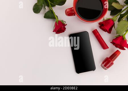 Smartphone, roter Lippenstift, Nagellack, Kaffee und Rosen auf weißem Hintergrund Stockfoto