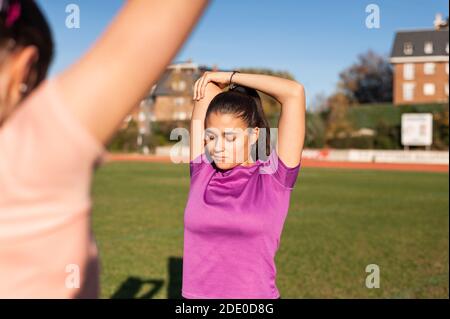 Zwei junge Frauen tun Stretching auf dem Gras eines Laufstrecke vor dem Sport Stockfoto