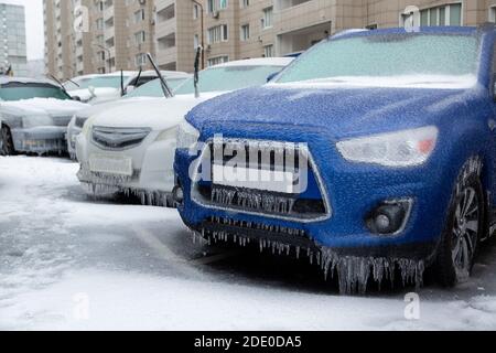 Der blaue SUV und andere Autos stehen in der Stadt gefroren und eisig vom Regen im Winter. Durch Eis blockiert. Stockfoto