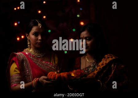 Zwei schöne indische bengalische Frauen in indischen traditionellen Kleid Anbetung mit Blumen in der Dunkelheit auf Diwali Abend. Indischer Lebensstil und Diwali Stockfoto