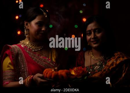 Zwei schöne indische bengalische Frauen in indischen traditionellen Kleid Anbetung mit Blumen in der Dunkelheit auf Diwali Abend. Indischer Lebensstil und Diwali Stockfoto