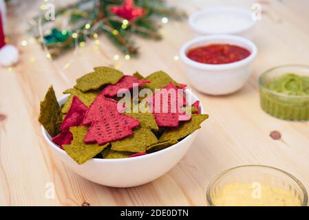 Weihnachtliche festliche Snacks. Grüne und rote Tortilla Chips Chips in Form eines Weihnachtsbaums in einer weißen Schüssel mit Salsa, Guacamole, Käse und sauer Stockfoto