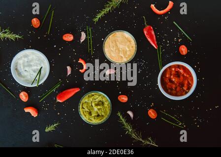 Draufsicht Schüsseln mit Mayo-Sauerrahm, Salsa, Guacamole, Käse-Dipping Saucen mit Zutaten und Gewürzen auf schwarzem Hintergrund. Dressing Dips für Stockfoto