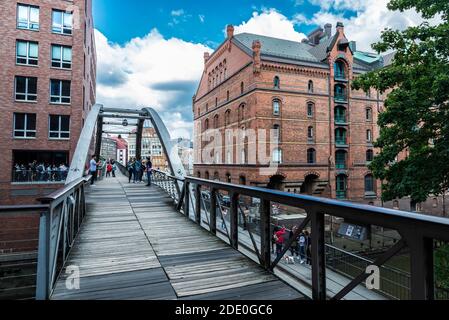 Hamburg, Deutschland - 21. August 2019: Fußgängerbrücke über einen Kanal mit Menschen und einem alten klassischen Lagerhaus in der HafenCity, Hamburg, Deutschland Stockfoto