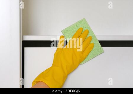 Hausfrau reinigt das Haus, wischt Staub mit einem Putzlappen. Hand in gelb Schutzhandschuh ist wischen weiße Möbel mit Lappen. Stockfoto