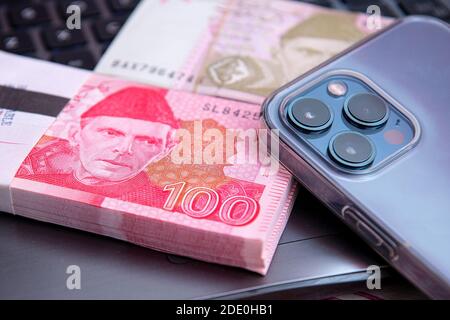 Pakistanische Währung 100 Rupien Banknote mit iphone 12 pro max. Geschäfts- und Finanzkonzept Stockfoto