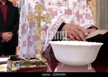 Das Kreuz im Vordergrund, aus der Nähe, während der Taufzeremonie in der orthodoxen Kirche mit dem Priester, der die Zeremonie durchführt. Stockfoto