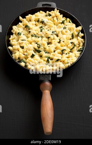 Hausgemachter Spinat Mac und Käse in einer gusseisernen Pfanne auf schwarzem Hintergrund, Seitenansicht. Stockfoto