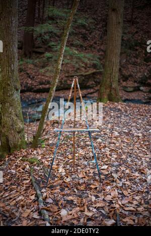 Eine KunstStaffelei in der Mitte des Waldes während der Herbstsaison mit Blättern zu Boden gefallen gefunden. Stockfoto