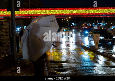 Madrid, Spanien. November 2020. Ein Mann, der mit einem Regenschirm bedeckt ist, um sich vor dem Regen zu schützen, macht mit seinem Handy ein Foto zu einer Brücke, die mit den Farben der spanischen Flagge beleuchtet ist und Teil der traditionellen Weihnachtsbeleuchtung ist. Der Stadtrat von Madrid hat in diesem Jahr mehr als einen Kilometer Lichter mit den Farben der spanischen Flagge installiert. Quelle: Marcos del Mazo/Alamy Live News Stockfoto