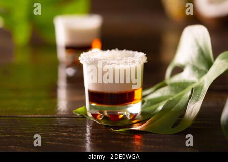 Tropische alkoholische Aufnahmen mit Kokosflocken, Monstera Blume mit Kokosnuss und Ananas auf braunem Holzhintergrund dekoriert Stockfoto