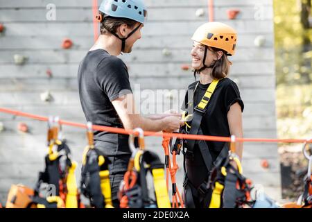 Männlicher Instruktor legt einer jungen Frau eine schützende Kletterausrüstung an Im Vergnügungspark im Freien Stockfoto