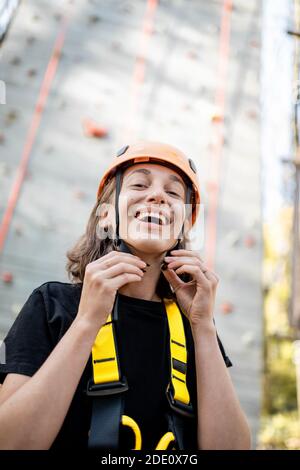 Porträt einer gut ausgerüsteten jungen Frau, die davor steht Der Kletterwand im Vergnügungspark Stockfoto