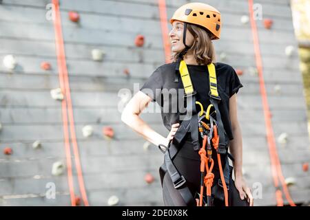 Porträt einer gut ausgerüsteten jungen Frau, die davor steht Der Kletterwand im Vergnügungspark Stockfoto