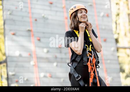 Porträt einer gut ausgerüsteten jungen Frau, die davor steht Der Kletterwand im Vergnügungspark Stockfoto