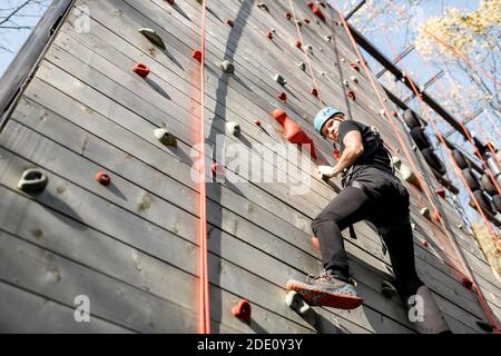 Gut ausgerüsteter Mann klettert die Wand im Freien im Park für Sportunterhaltung Stockfoto