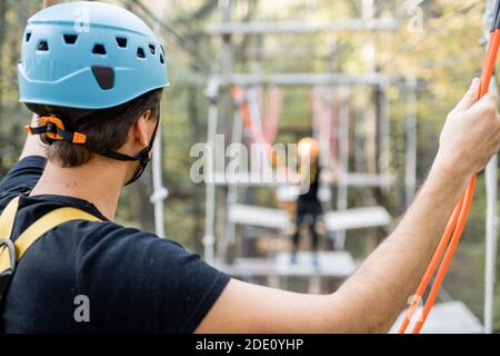Gut ausgerüsteter Mann mit aktiver Erholung, Klettern in einem Seilpark mit Hindernissen im Wald, Nahaufnahme von der Rückseite Stockfoto