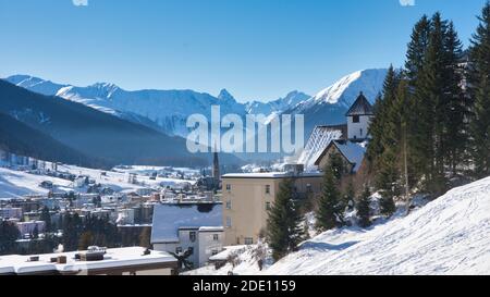 Verschneite Stadt in den Bergen. Davos Graubünden Schweiz. Höchste Stadt Europas, Winterlandschaft mit Blick auf die Alpen und Kirchturm Stockfoto