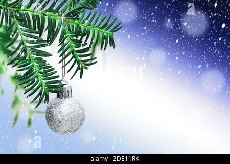 Silberner Weihnachtsball auf grünen Tannenzweig auf blauem schneebedecktem Hintergrund. Weihnachtsdekoration. Weihnachtskarte. Speicherplatz kopieren. Stockfoto