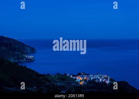 Die Fischerdörfer Corniglia (vorne) und Manarola (hinten) in Cinque Terre, Italien, beleuchtet in der Dämmerung während der blauen Stunde mit dem Mittelmeer Stockfoto