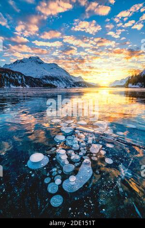 Wolken am brennenden Himmel bei Sonnenuntergang am Piz Da La Margna und Eisblasen im Sils-See, Engadin, Graubünden, Schweiz, Europa Stockfoto