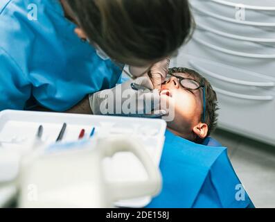 Stock Foto von unerkannt professionelle Zahnmediziner trägt Gesichtsmaske aufgrund covid19 tun Reinigung Behandlung, um einen kleinen Jungen. Stockfoto