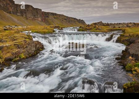 Eine klassische isländische Landschaft, ein Fluss fließt entlang der Basis einer Klippe, der Fossalar River, in der Nähe von Kirkjubaejarklaustur, Island, Polarregionen Stockfoto