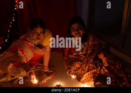 Zwei schöne indische bengalische Frauen in indischen traditionellen Kleid Beleuchtung Diwali Lampen sitzen auf dem Boden am Diwali Abend. Indischer Lebensstil Stockfoto