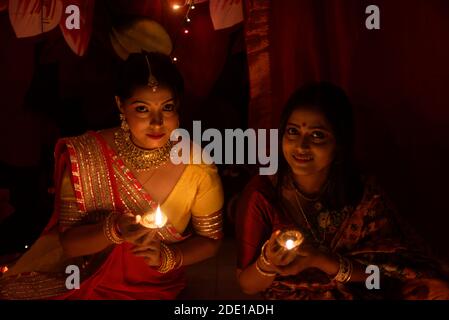 Zwei schöne indische bengalische Frauen in indischen traditionellen Kleid Beleuchtung Diwali Lampen sitzen auf dem Boden am Diwali Abend. Indischer Lebensstil Stockfoto