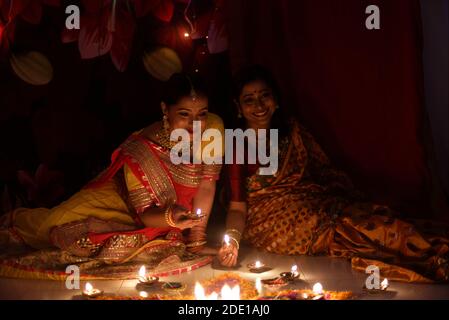 Zwei schöne indische bengalische Frauen in indischen traditionellen Kleid Beleuchtung Diwali Lampen sitzen auf dem Boden am Diwali Abend. Indischer Lebensstil Stockfoto