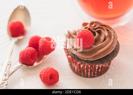 Schokolade Cupcakes mit Schokolade Buttercreme Zuckerguss dekoriert mit frischen Himbeeren close up auf weißem Hintergrund, selektive Fokus Stockfoto