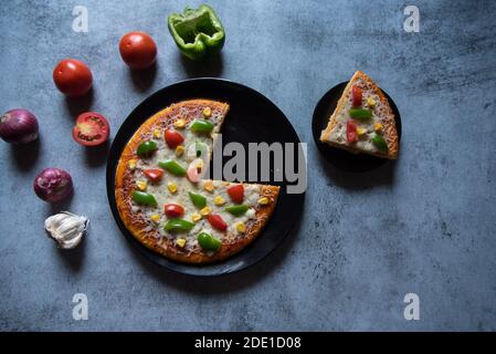 Pizza und ein Stück Pizza auf einem schwarzen Teller Stockfoto