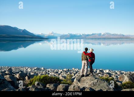 Pärchen, die am Ufer des Pukaki-Sees stehen und den Mt Cook im klaren Wasser beobachten. Stockfoto