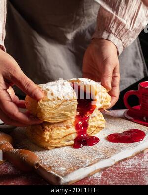 Weibliche Hände backt einen Puff mit Pflaume oder rote Johannisbeermarmelade auf dem Tisch. Stockfoto