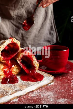 Weibliche Hände backt einen Puff mit Pflaume oder rote Johannisbeermarmelade auf dem Tisch. Stockfoto