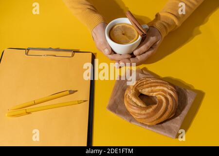 Hände Halten Tasse Tee oder Glühwein in der Nähe von Resume Sheet und Kuchen auf der Fortuna Gold Gelb Farbe Hintergrund, Draufsicht. Stockfoto