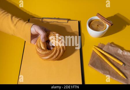 Hand halten Kuchen in der Nähe von Tasse Tee oder Glühwein und Resume Sheet auf der Fortuna Gold Gelb Farbe Hintergrund, Draufsicht. Stockfoto